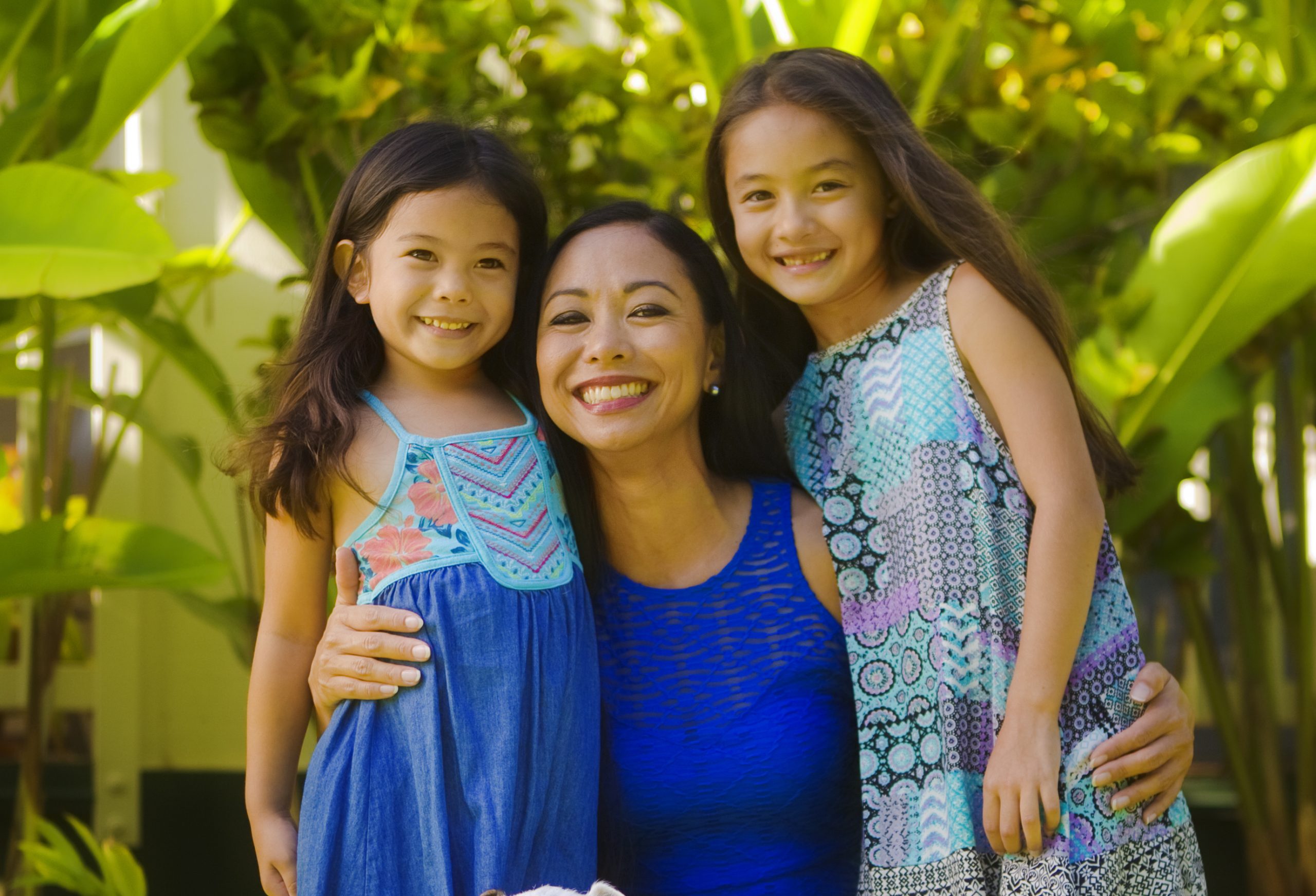 Portrait of a Hawaiian Polynesian family outdoor in their backyard. Two young girls with their mother and family pet dog, smiling and looking at camera full body group portrait.